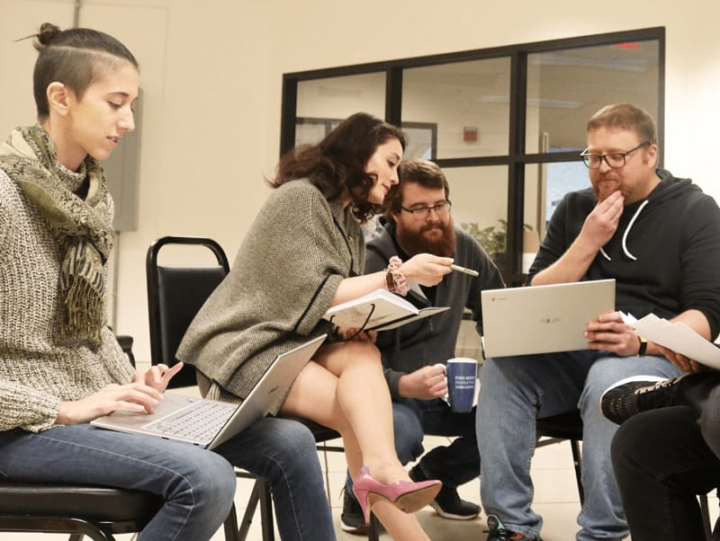 Four individuals collaborating on a writing project using their notebooks and laptops